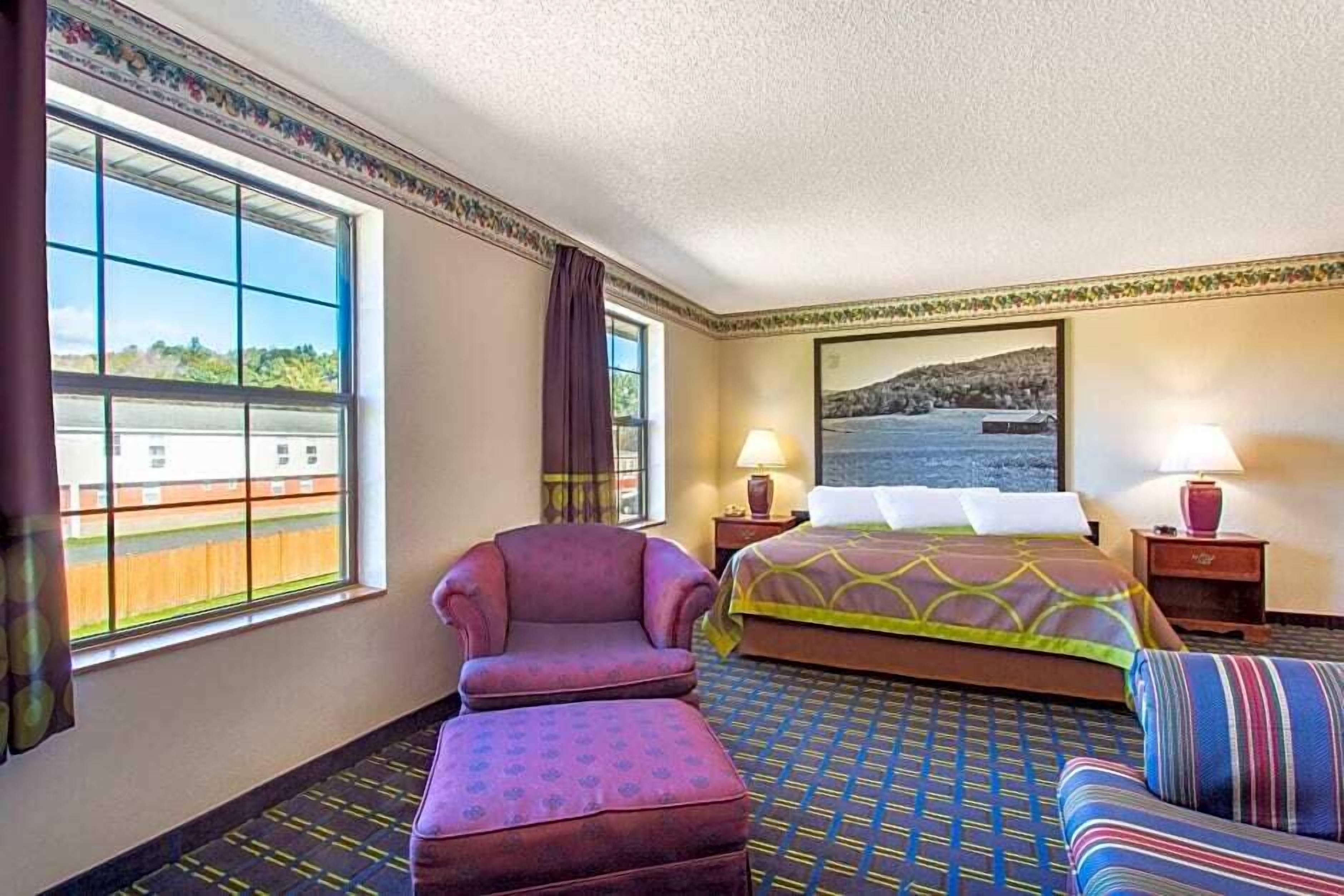 A hotel room with a large window, a bed, a chair, a sofa, and a painting on the wall.