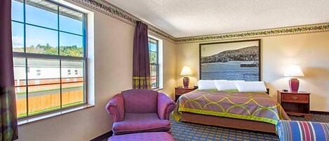 A hotel room with a large window, a bed, a chair, a sofa, and a painting on the wall.