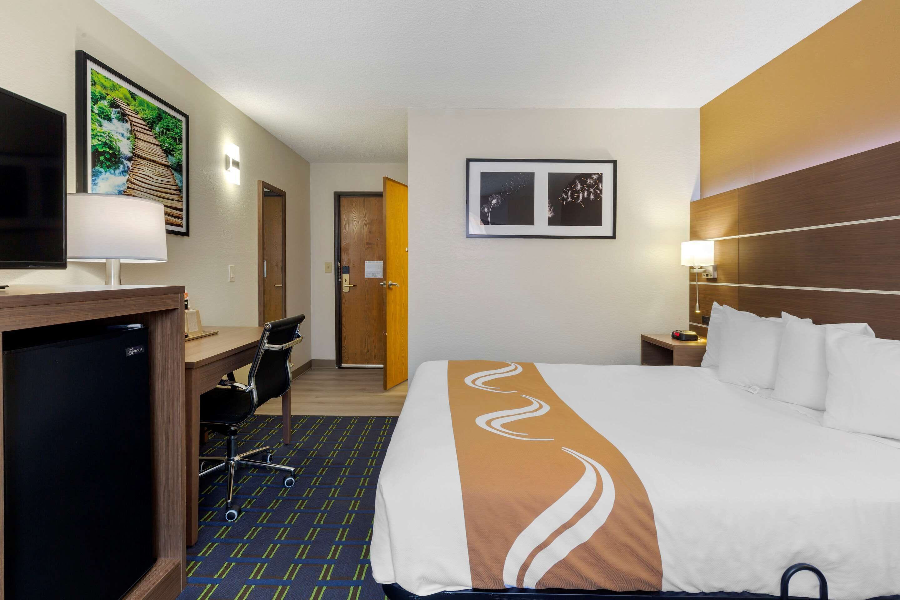 Habitación de hotel con cama, escritorio, silla, televisión y una puerta que da a otra habitación.