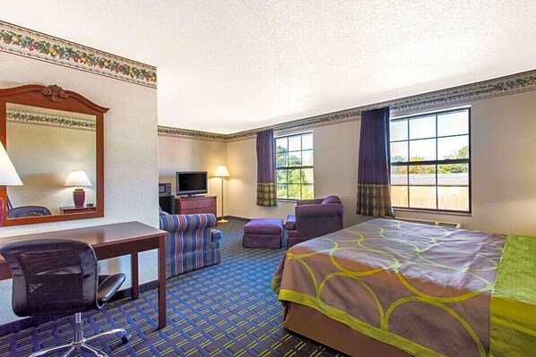 A hotel room with a bed, a desk with a chair, a television, and a window with curtains.