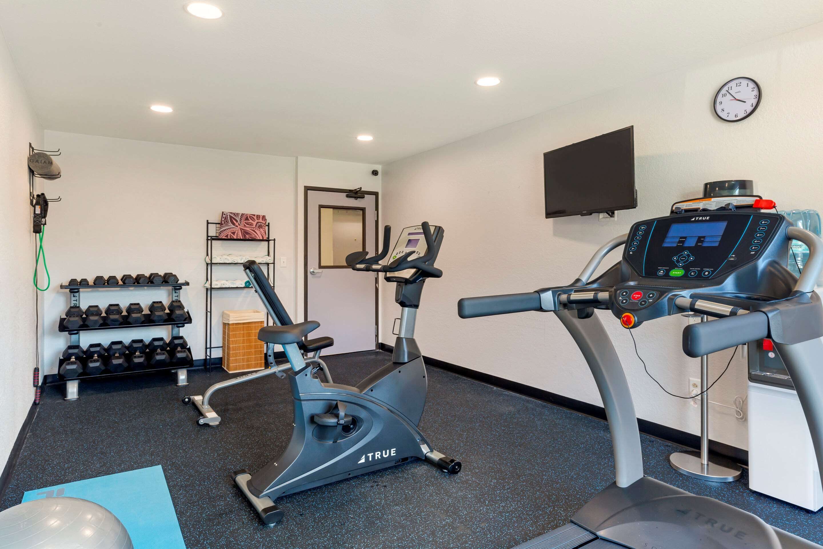 A gym with two exercise bikes, a wall-mounted TV, and a clock.