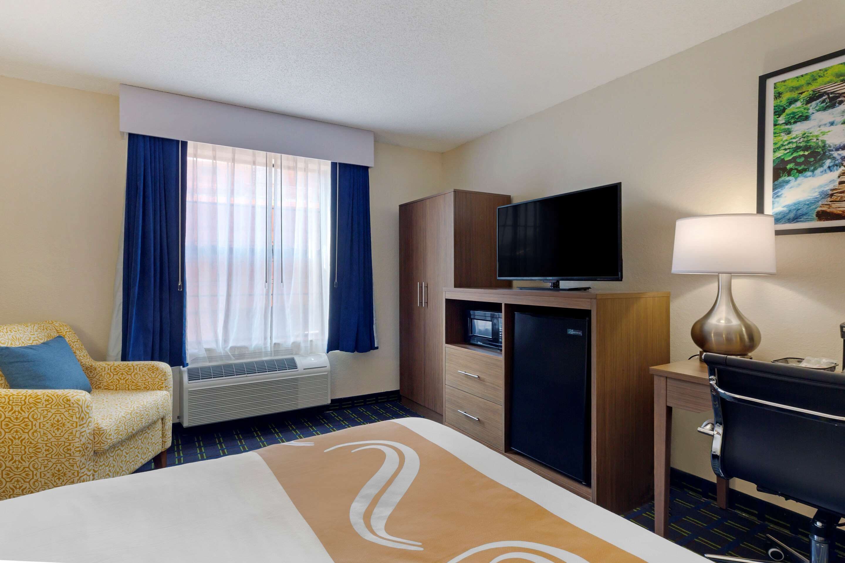 A hotel room with a bed, a desk, a television, a lamp, a wardrobe, and a window with curtains.