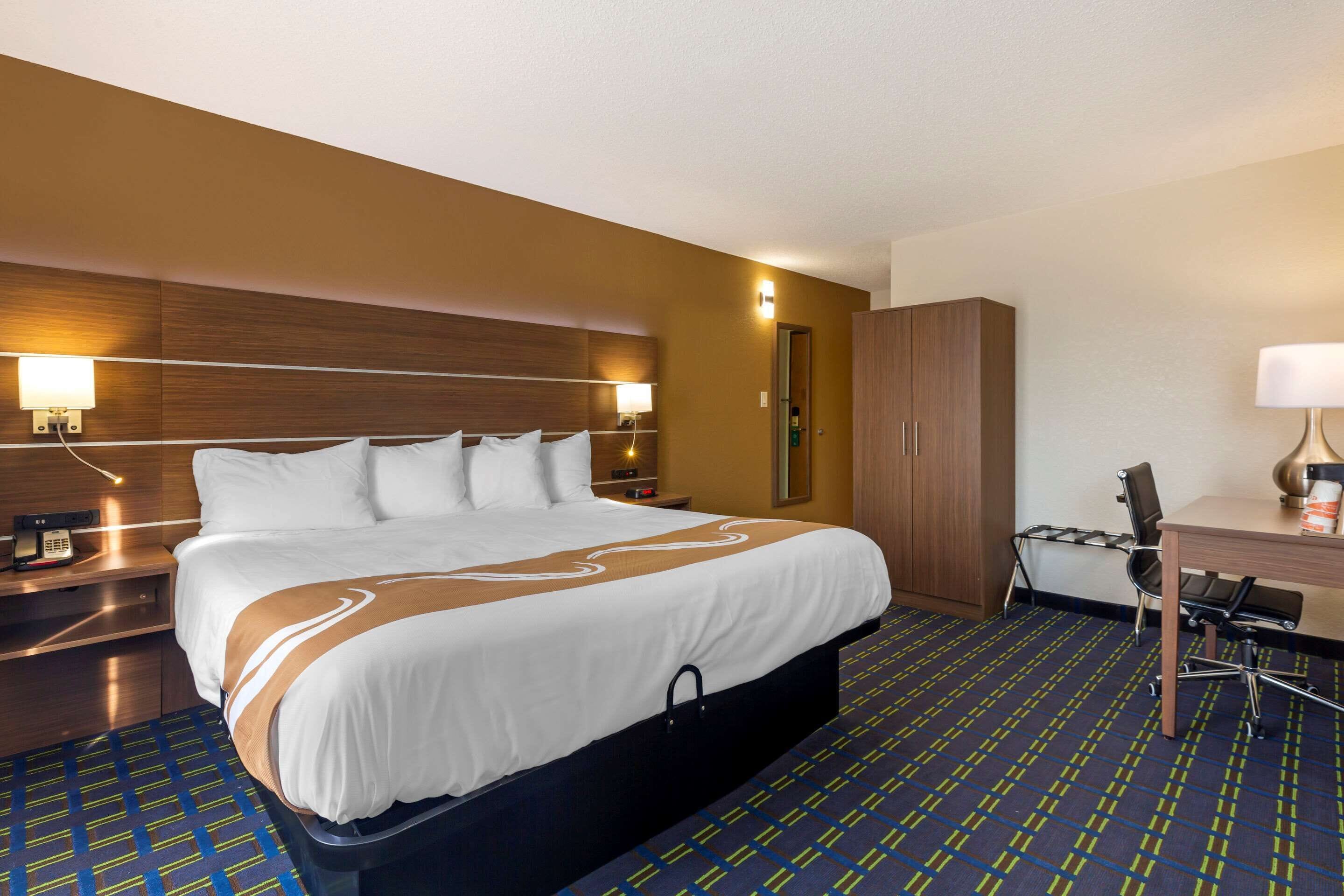 A hotel room with a large bed, a desk, a chair, a wardrobe, and two bedside lamps.