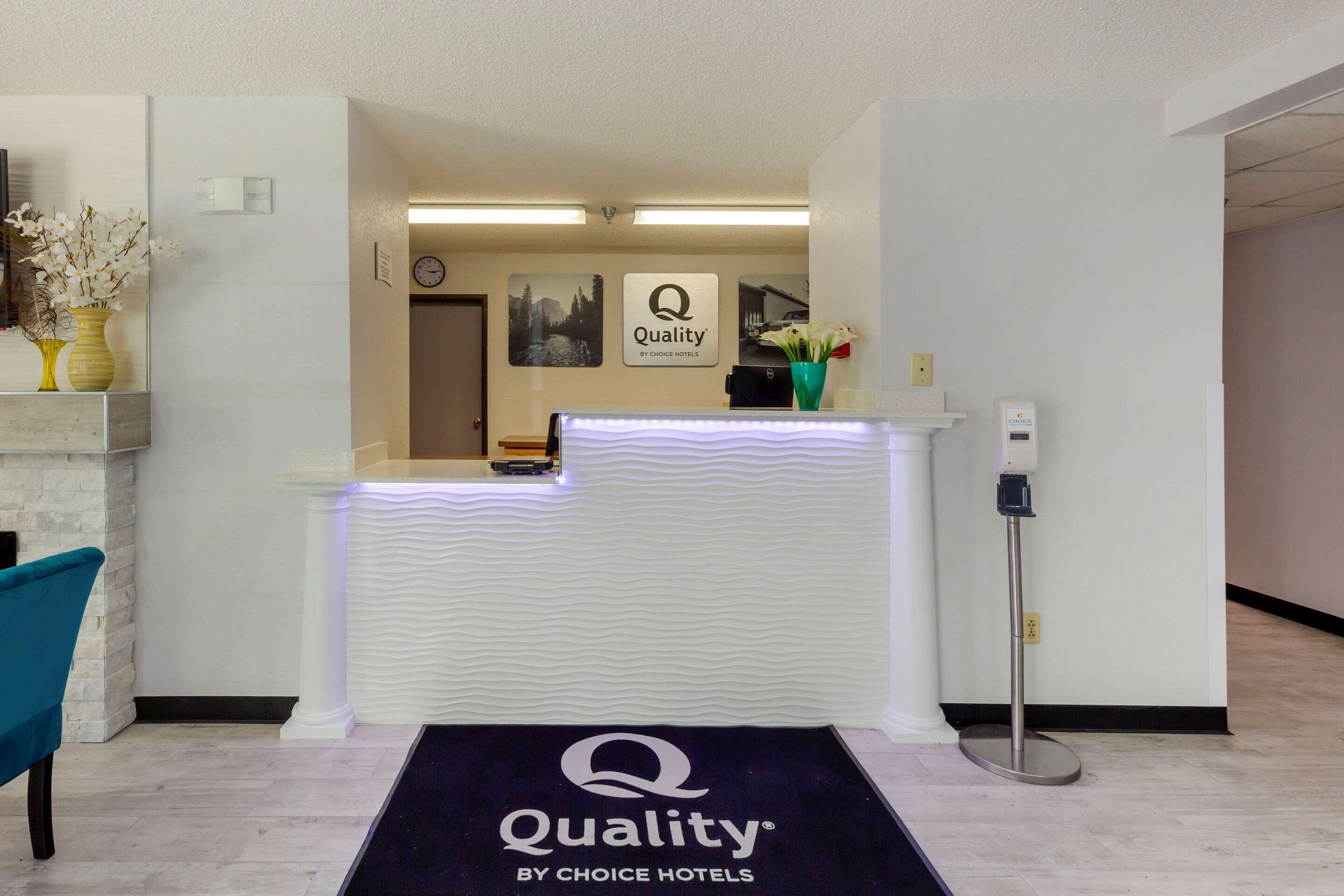 A hotel reception area with a reception desk, a clock, and a sign that reads "Quality by Choice Hotels".