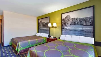 Una habitación de hotel con dos camas, cada una con una colcha estampada, una mesita de noche con lámpara y un cuadro grande en la pared.