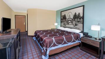A hotel room with a bed, a desk with a television, a nightstand, a lamp, and a framed picture on the wall.
