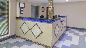 Un área de recepción con mostrador, certificados enmarcados, un reloj y piso a cuadros.