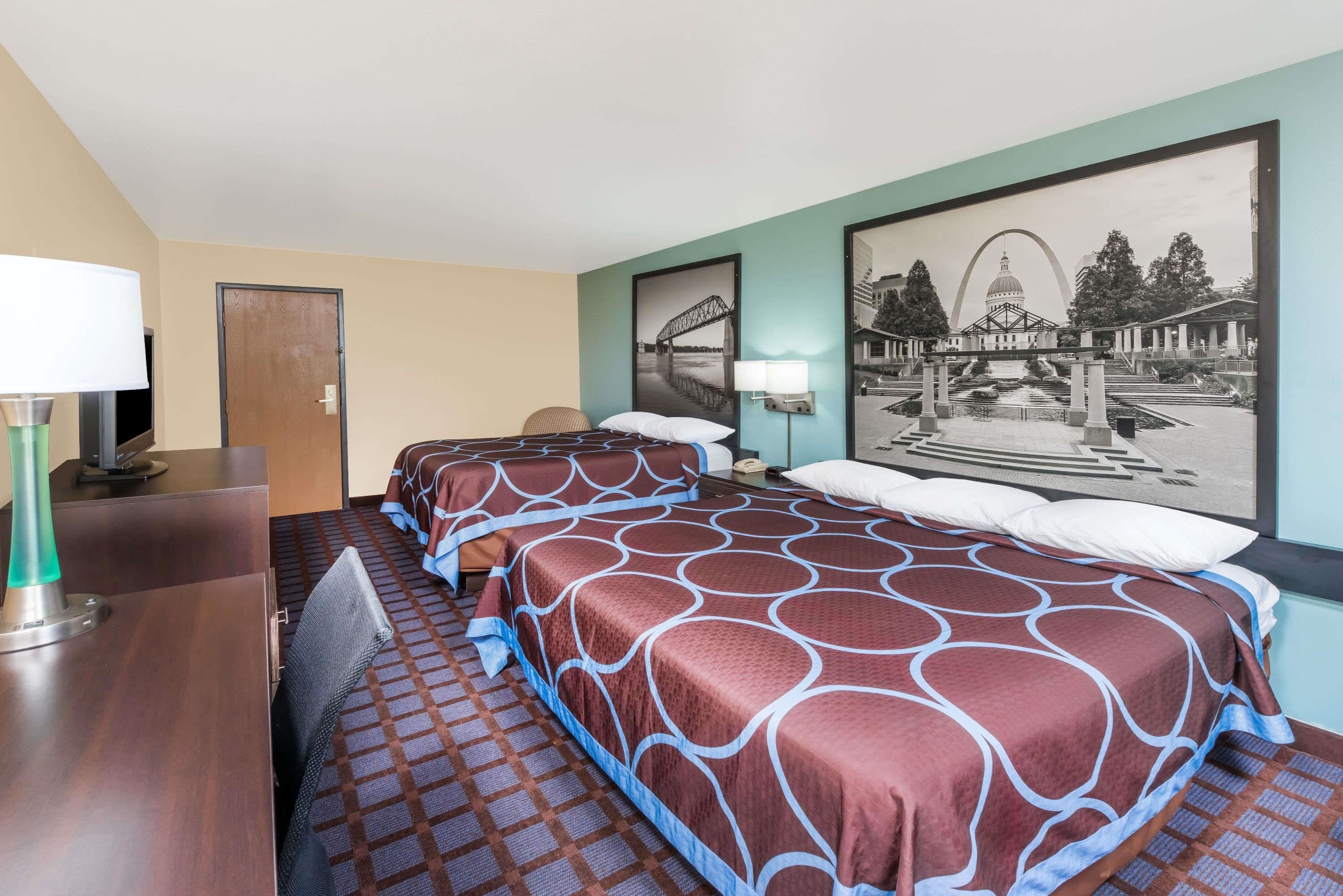 A hotel room with two beds, a desk, a chair, a lamp, and a large framed picture on the wall.