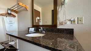 Un baño con lavamanos de granito, un espejo, un perchero para toallas y un teléfono.