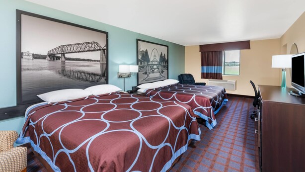 Habitación de hotel con dos camas, un escritorio con computadora, una silla, un televisor y dos lámparas fijadas a la pared.