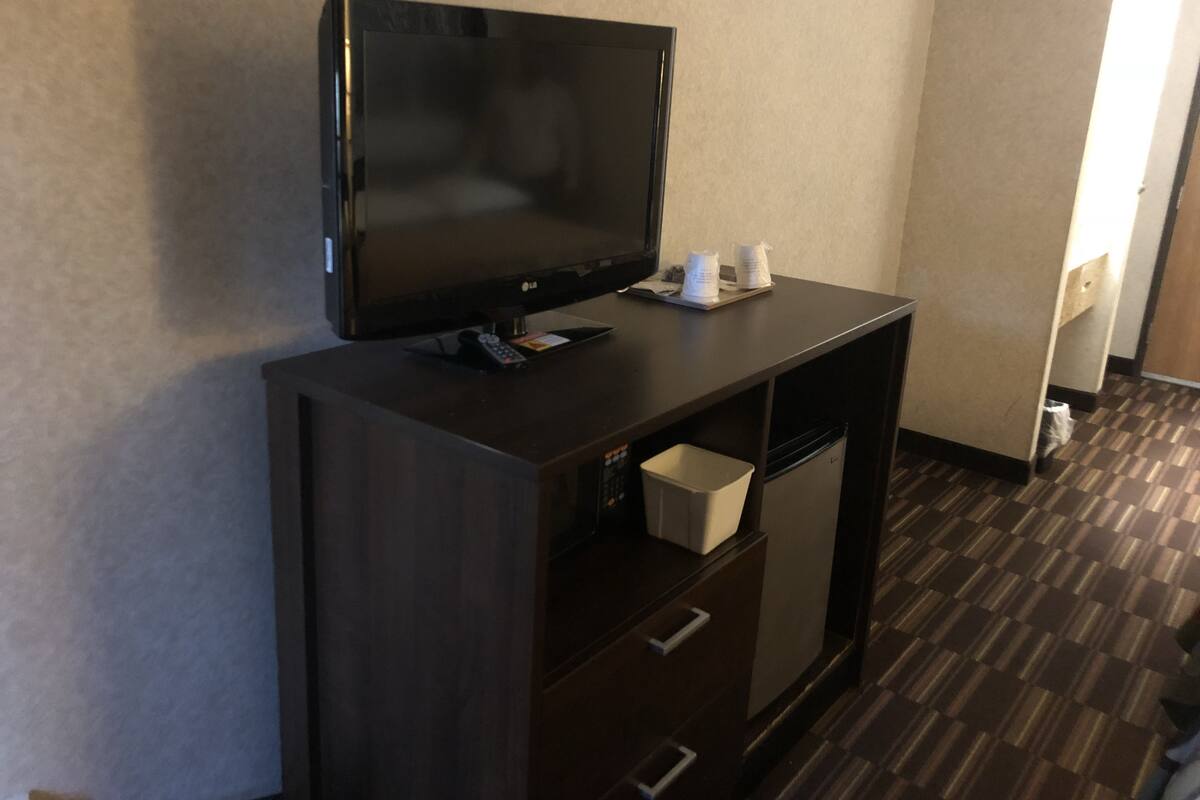 Un meuble TV en bois foncé, sur lequel est posée une télévision à écran plat, une télécommande et deux tasses.