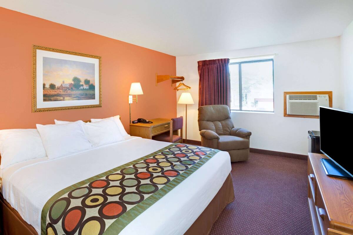 Een hotelkamer met een groot bed, een stoel, een bureau met een televisie, een lamp en een schilderij aan de muur.