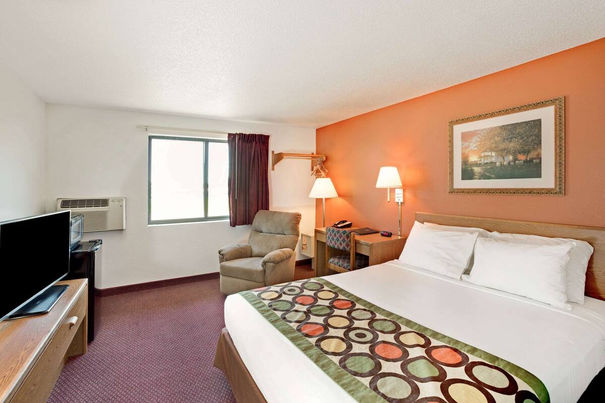 Een hotelkamer met een bed, een televisie, een bureau, een stoel en een raam.