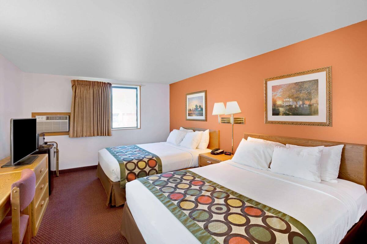 Een hotelkamer met twee bedden, een bureau, een televisie en een raam met gordijnen.