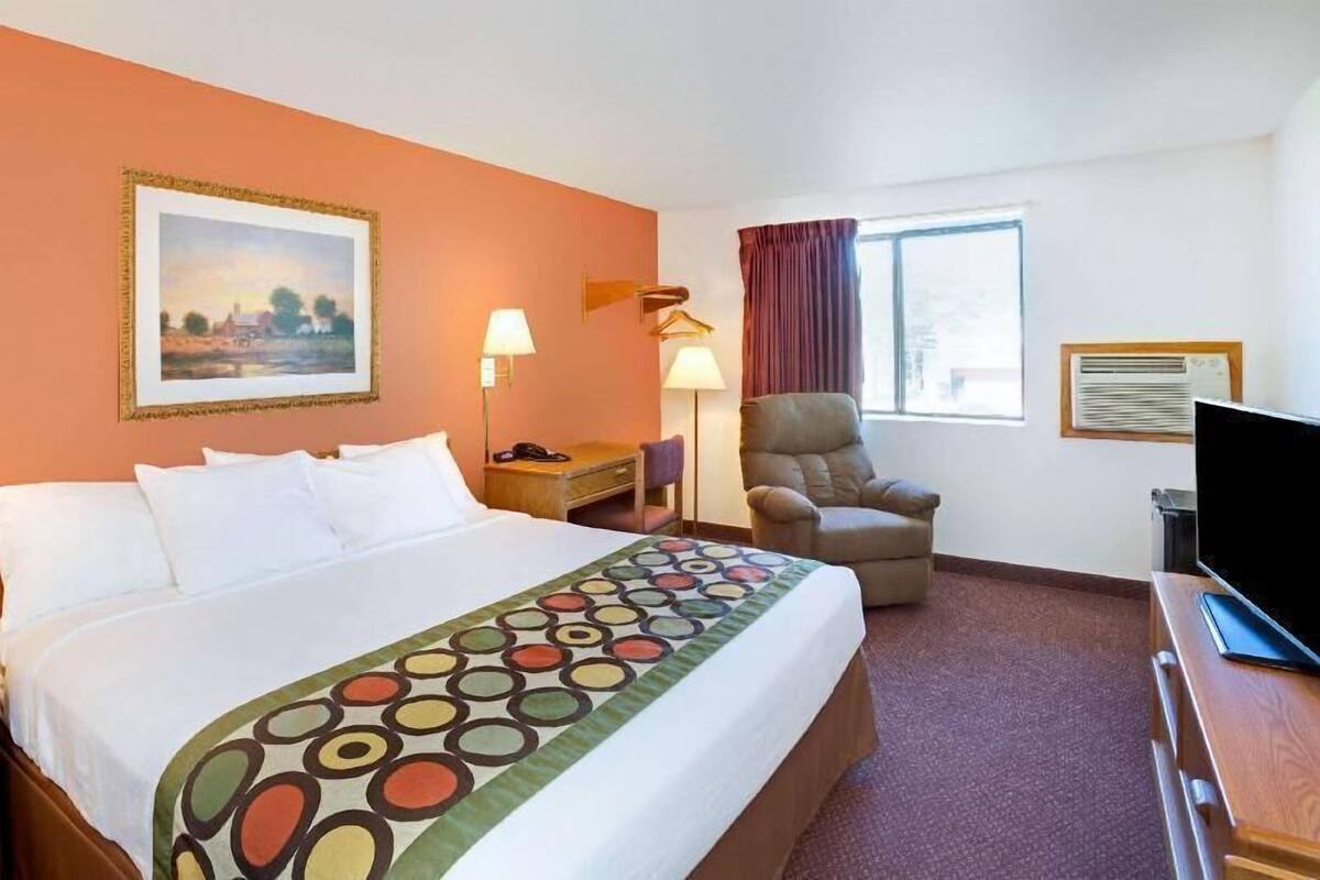 Een hotelkamer met een bed, een stoel, een bureau met een televisie, een lamp en een schilderij aan de muur.