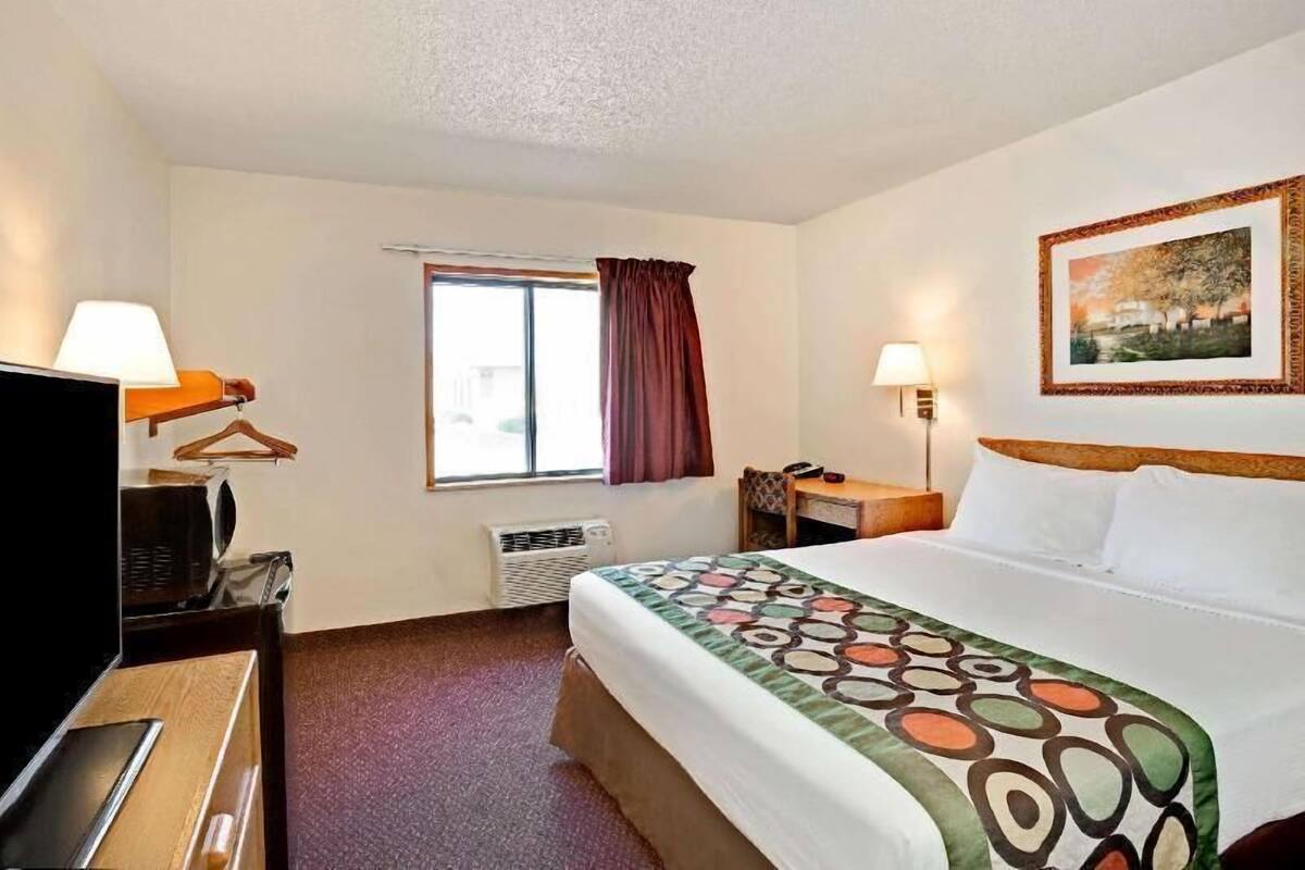 Een hotelkamer met een bed, een bureau, een stoel, een televisie, een raam met gordijnen en een wandlamp.