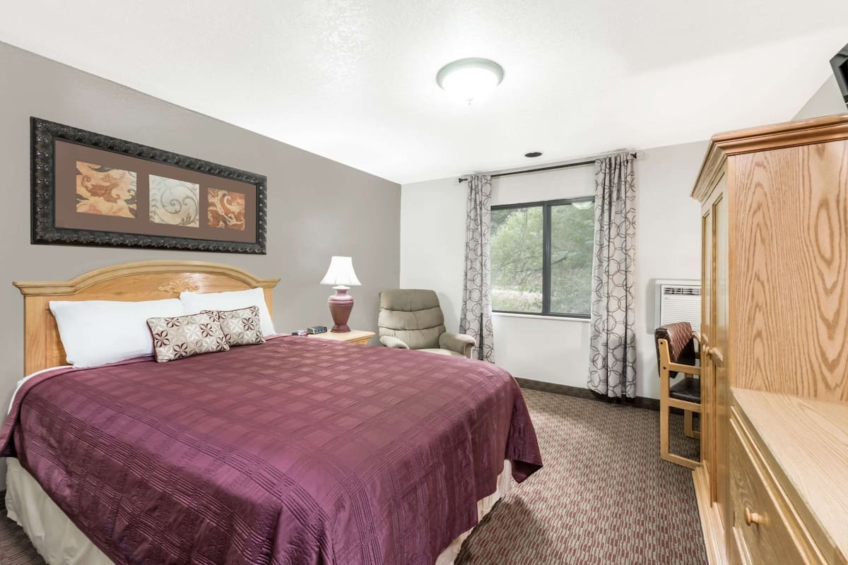 Un dormitorio ordenado con una cama grande, una silla, un aparador y una ventana con cortinas.