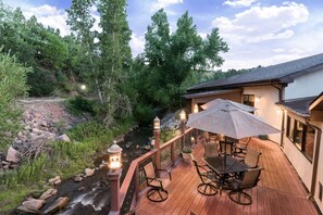 Une terrasse en bois, dotée de mobilier d’extérieur et offrant une vue sur un ruisseau.