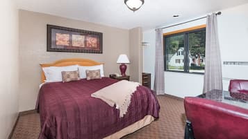 A hotel room with a large bed, a desk with a chair, a lamp, and a window with curtains.
