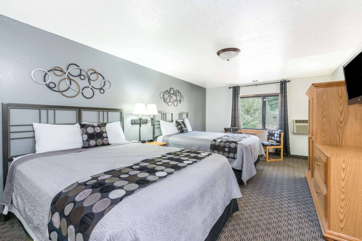 Habitación de hotel con dos camas, un armario de madera, un escritorio con silla y una ventana con cortinas.