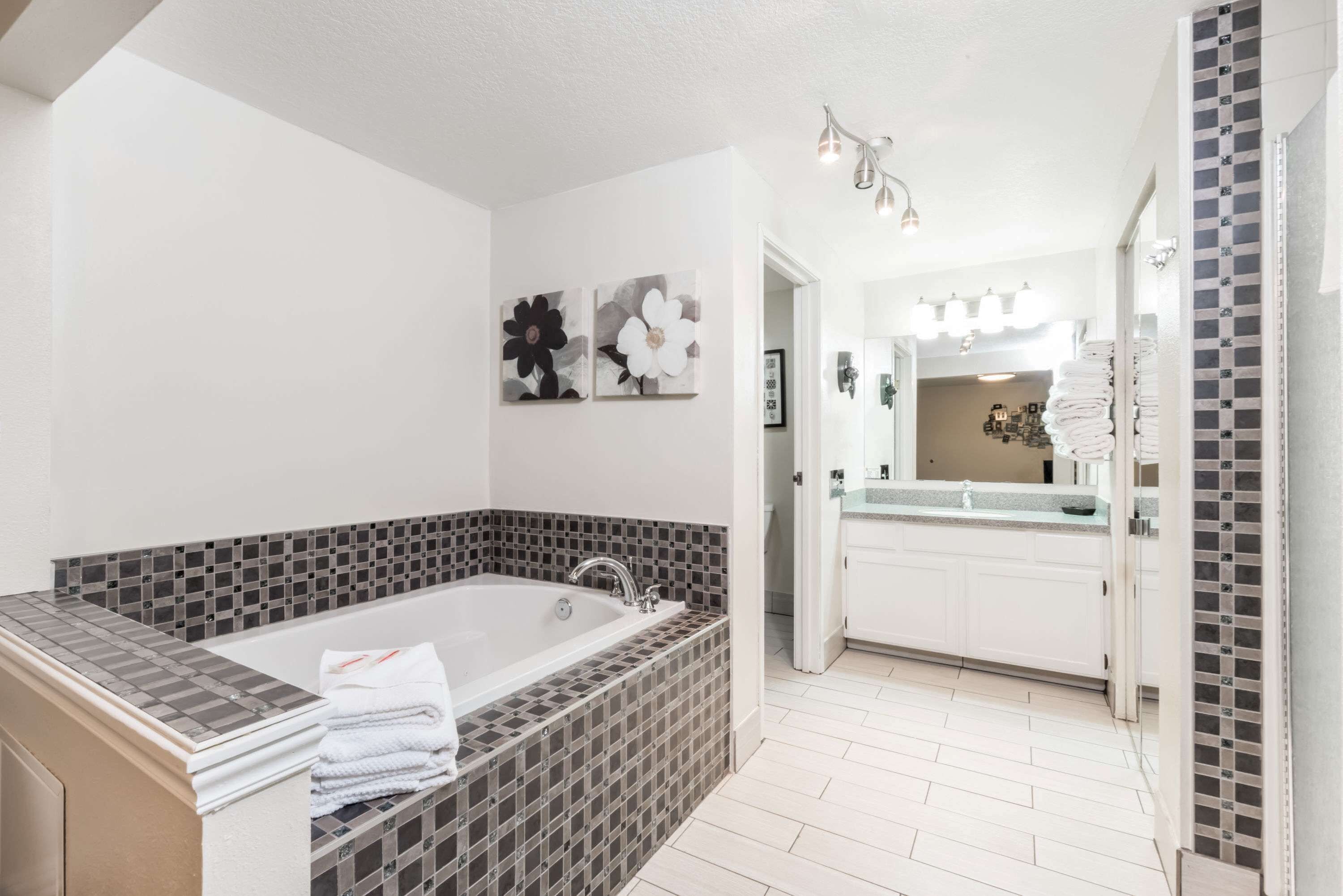 Une salle de bain moderne avec une grande baignoire, des meubles blancs et un sol carrelé.
