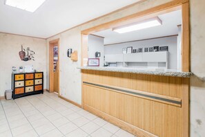 A reception area with a wooden reception desk, a tiled floor, a small cabinet with drawers, and a wall-mounted shelf with framed certificates. - Super 8 by Wyndham Deadwood / Black Hills Area (Deadwood)