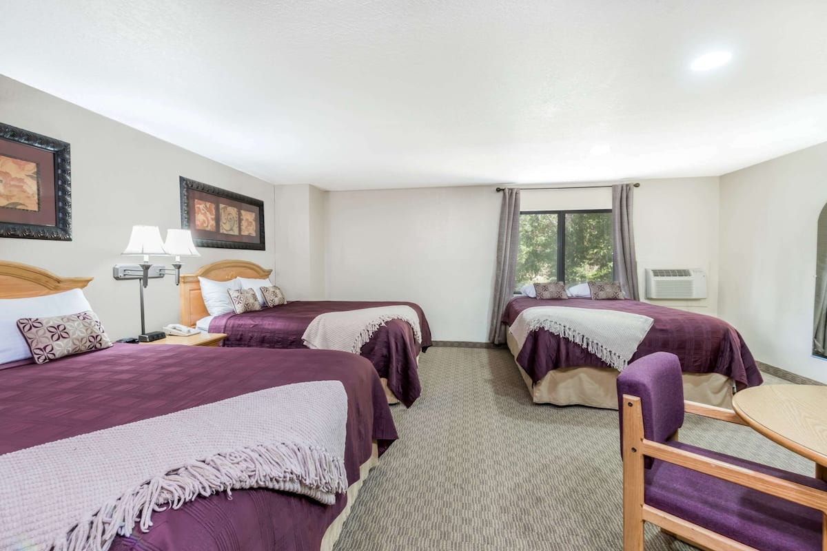 Una habitación de hotel con dos camas, un escritorio, una silla, una lámpara y un ventanal con cortinas.