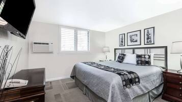 Une chambre à coucher avec un lit, des tables de chevet, une télévision et une fenêtre avec des stores.