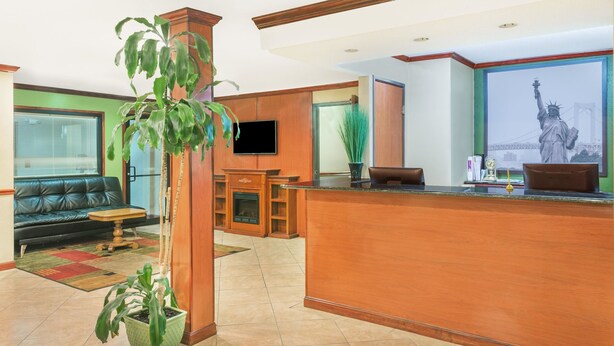 A hotel lobby with a reception desk, a television mounted on the wall, a sofa, a fireplace, and a large window with a statue view. - Super 8 by Wyndham Tilton/Lake Winnipesaukee (Tilton)