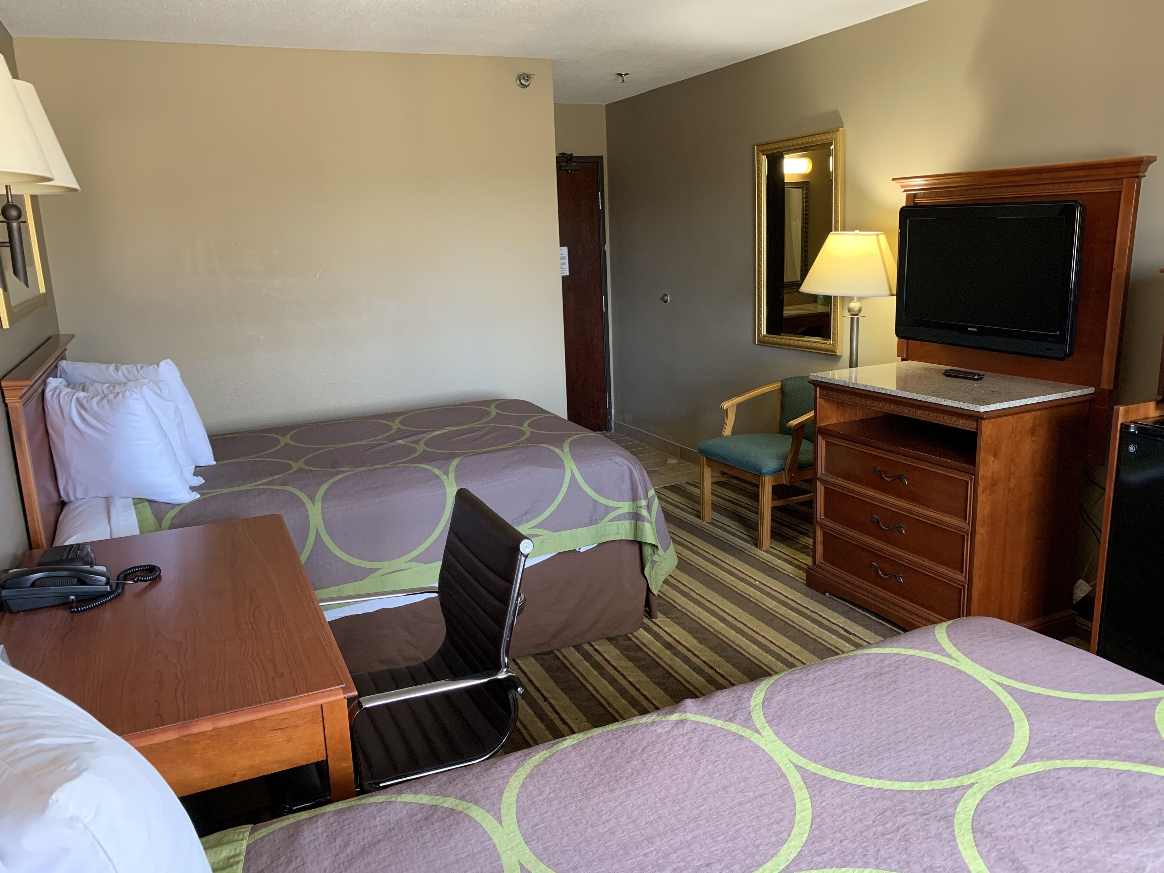 A hotel room with two beds, a desk, a chair, a television, and a mirror.