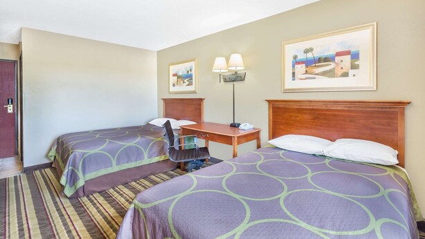 Une chambre d’hôtel avec deux lits, un bureau, une chaise, une lampe et deux tableaux au mur.