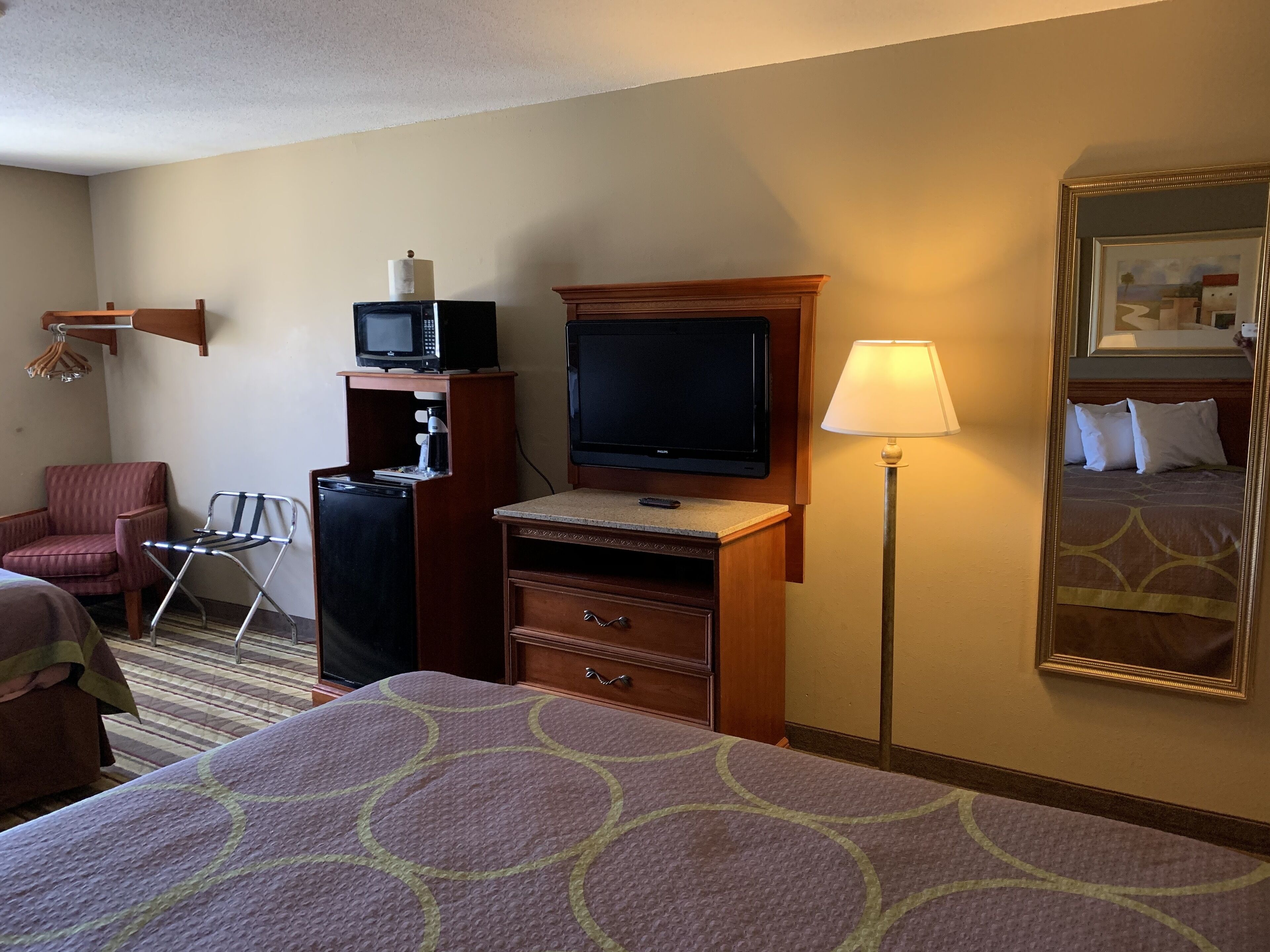 A hotel room with a bed, a desk with a television, a chair, a lamp, and a mirror.