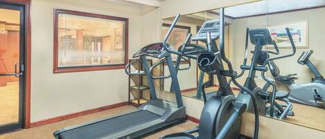 A gym with treadmills, elliptical machines, and a mirrored wall.