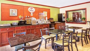 A restaurant with a breakfast counter, multiple tables and chairs, and a kitchen area. - Super 8 by Wyndham Tilton/Lake Winnipesaukee (Tilton)
