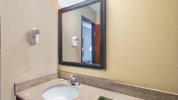 A bathroom with a granite countertop sink, a mirror with a wooden frame, and a hair dryer mounted on the wall.