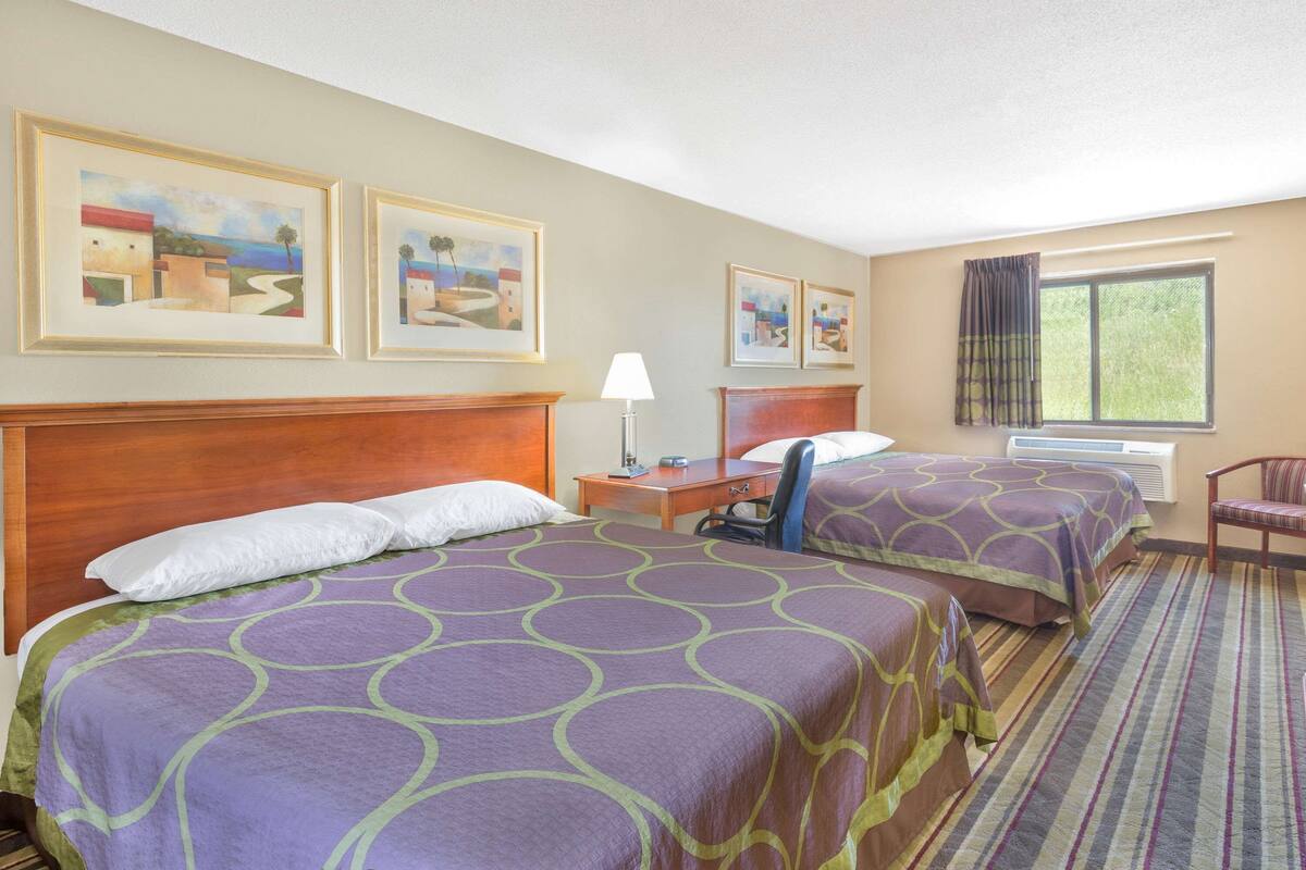A hotel room with two beds, a desk, a chair, and a window with curtains.