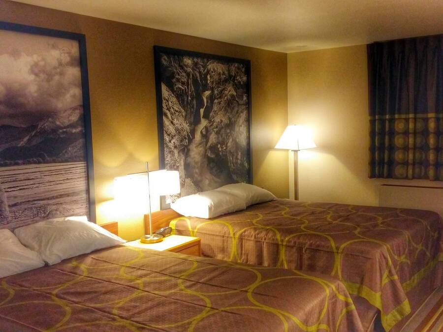 A hotel room with two beds, a nightstand, a lamp, and a large painting on the wall.
