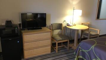 A hotel room with a TV, a desk with a telephone, a chair, a bed, and a lamp.