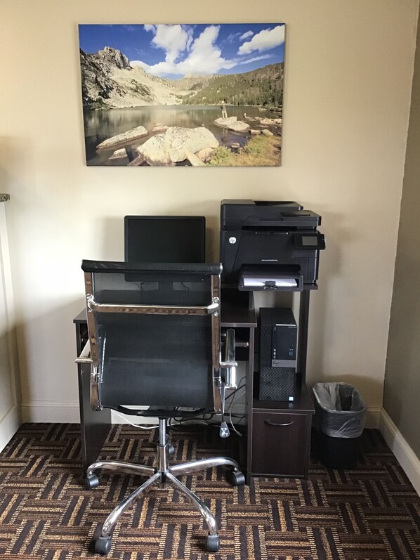 Un espacio de trabajo en casa con escritorio, silla, impresora y un cuadro con paisaje en la pared.
