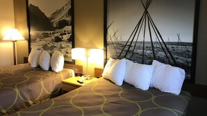 Habitación de hotel con dos camas, una mesita de noche con lámparas y dos cuadros grandes en la pared.