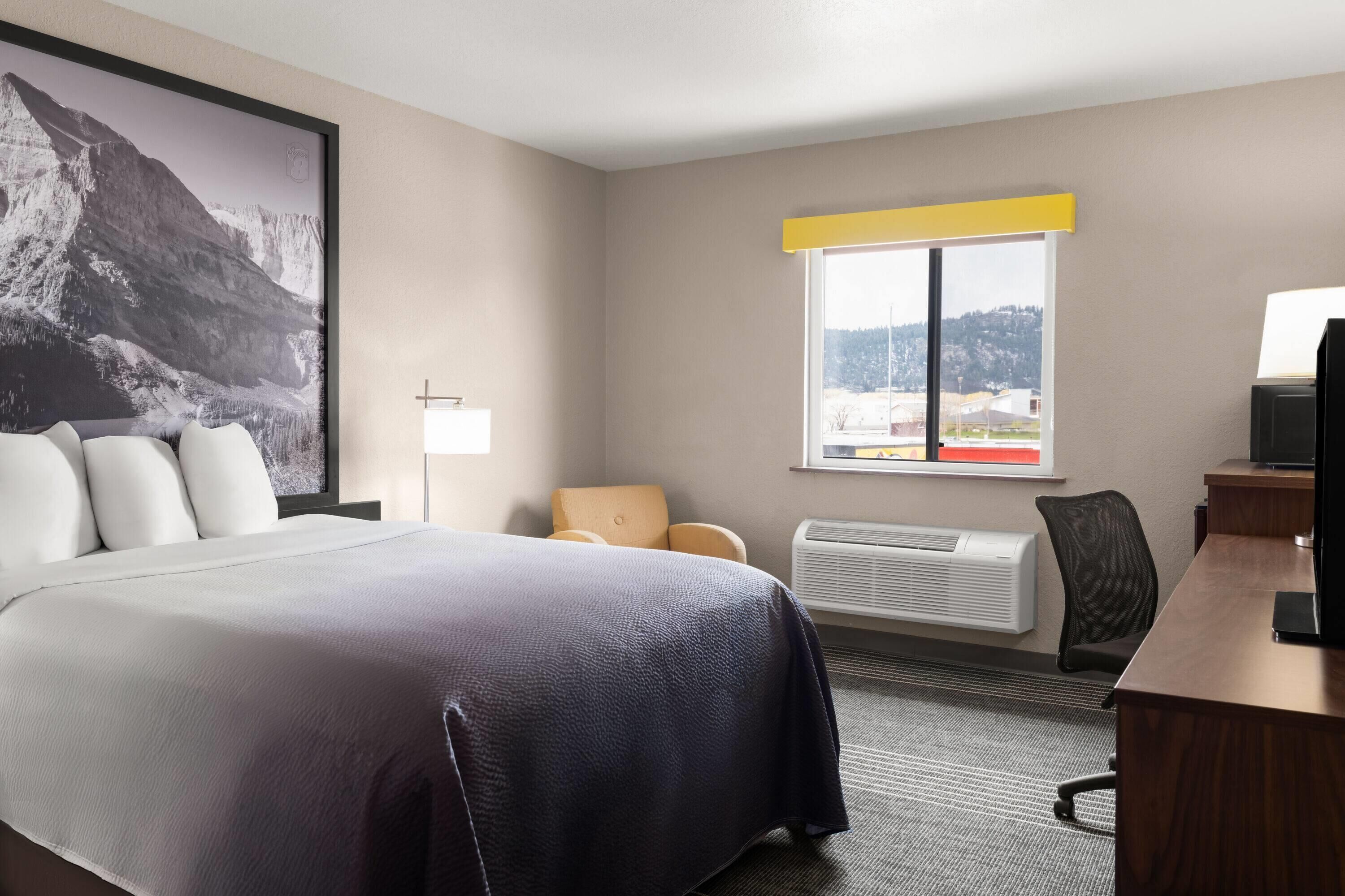 Habitación de hotel con una cama grande, un escritorio, una silla, un ventanal con vistas y una obra de arte colgada.