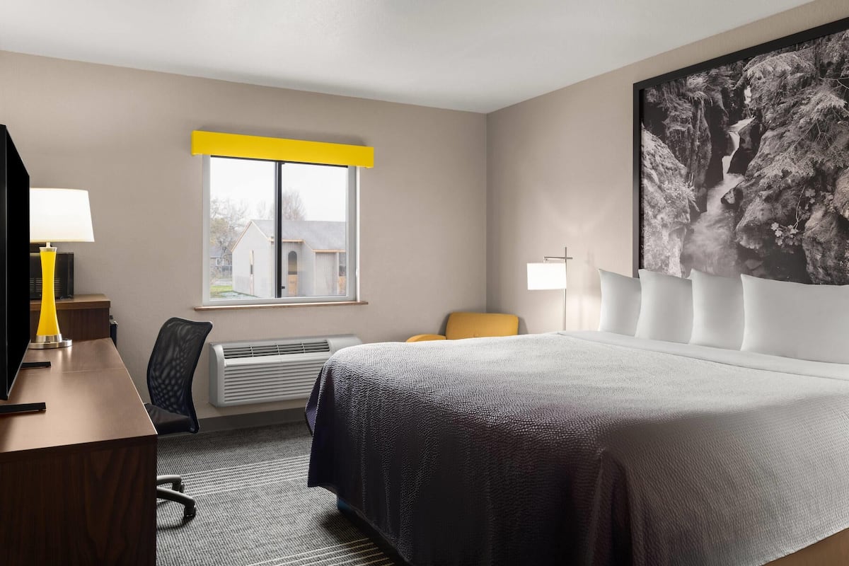 Quarto de hotel com cama, escrivaninha, cadeira, janela e obras de arte na parede.