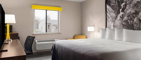 Habitación de hotel con cama, escritorio, silla, ventana y una obra de arte en la pared.