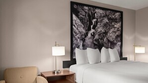A hotel room with a bed, a nightstand with a lamp, a chair, and a large framed picture on the wall. - Super 8 by Wyndham Kalispell Glacier National Park (Kalispell)