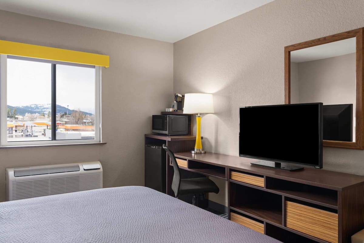 Quarto de hotel com cama, escrivaninha com TV, luminária, poltrona, micro-ondas e vista para a cidade.
