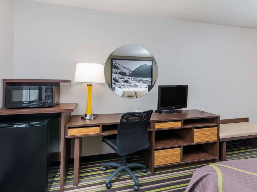 Quarto de hotel com uma escrivaninha de madeira, uma cadeira de escritório preta, micro-ondas, televisão e um frigorífico pequeno.