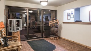 A reception area with a wooden reception desk, a 'HOWDY' sign, a metal gate, and a doormat. - Super 8 by Wyndham Kalispell Glacier National Park (Kalispell)