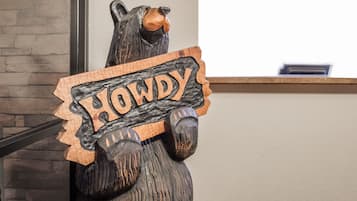 Escultura de urso de madeira segurando uma placa com a palavra 'HOWDY'.