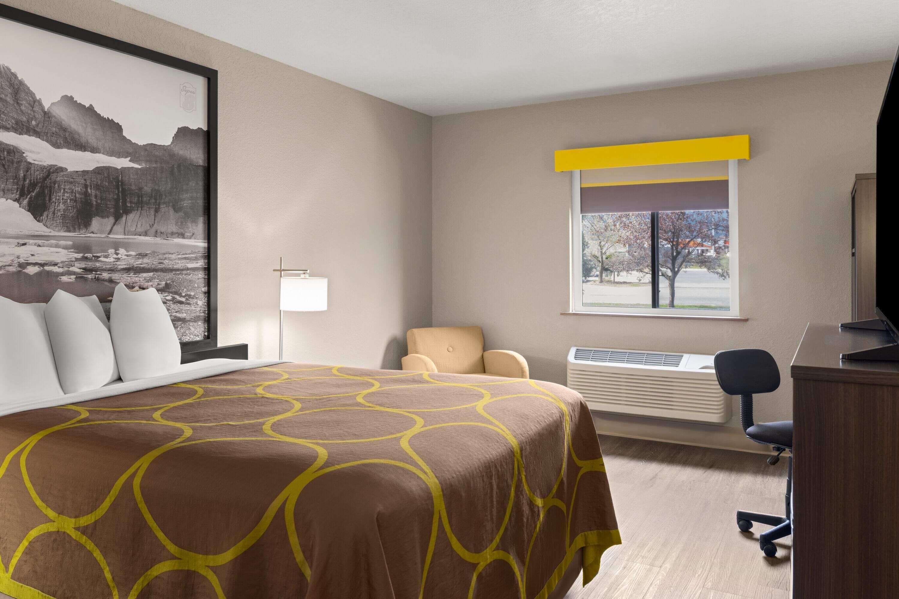 A hotel room with a bed, a desk, a chair, a window with a view, and a mounted TV.