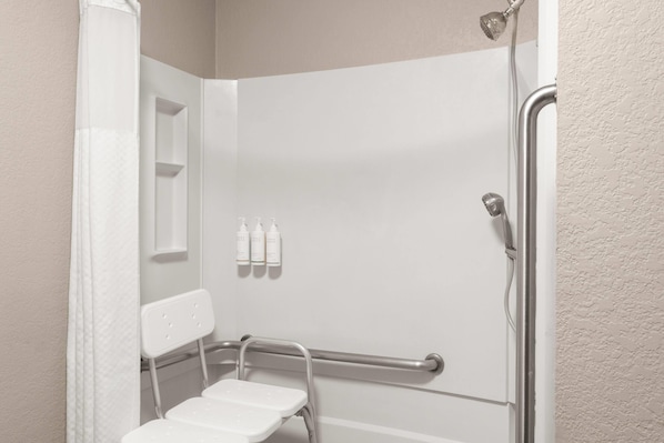 Un baño con ducha, una silla blanca y tres botellas en la pared.
